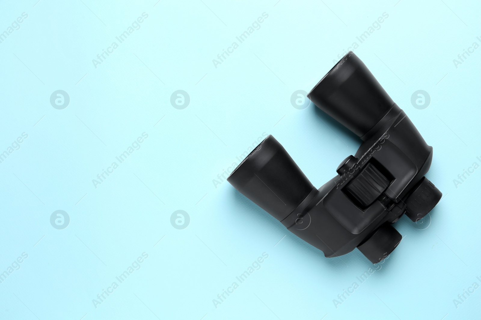 Photo of Modern binoculars on light blue background, top view. Space for text