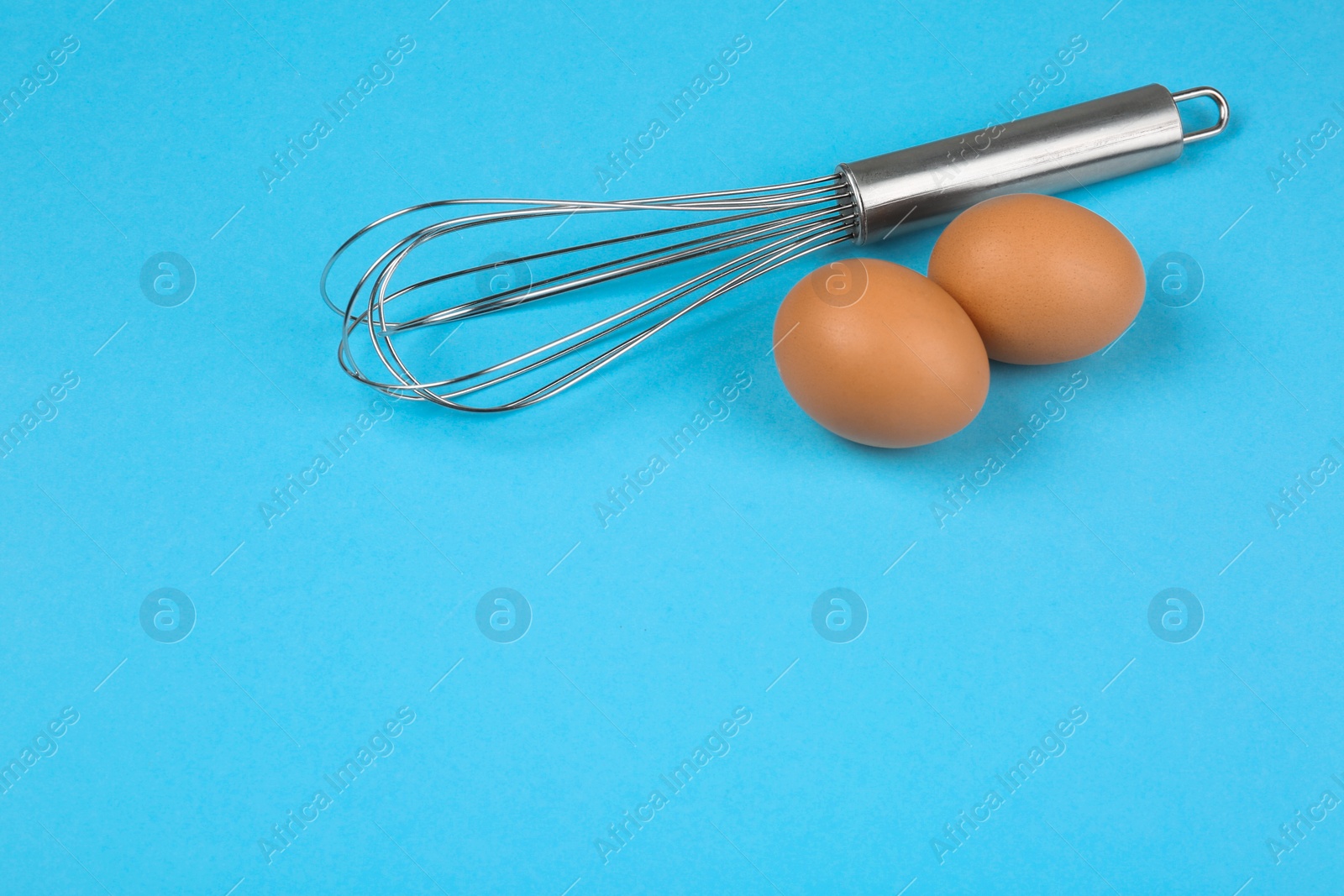 Photo of Raw eggs and whisk on light blue background, space for text. Baking pie