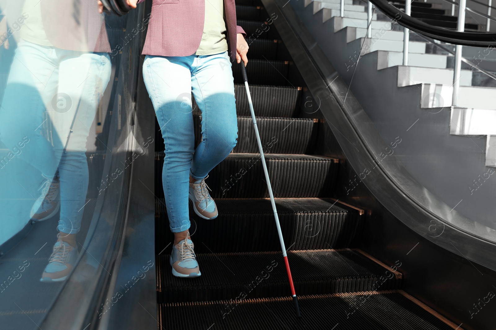 Photo of Blind person with long cane on escalator indoors