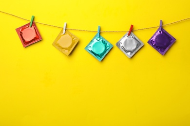 Photo of Colorful condoms hanging on clothesline against yellow background, space for text. Safe sex concept