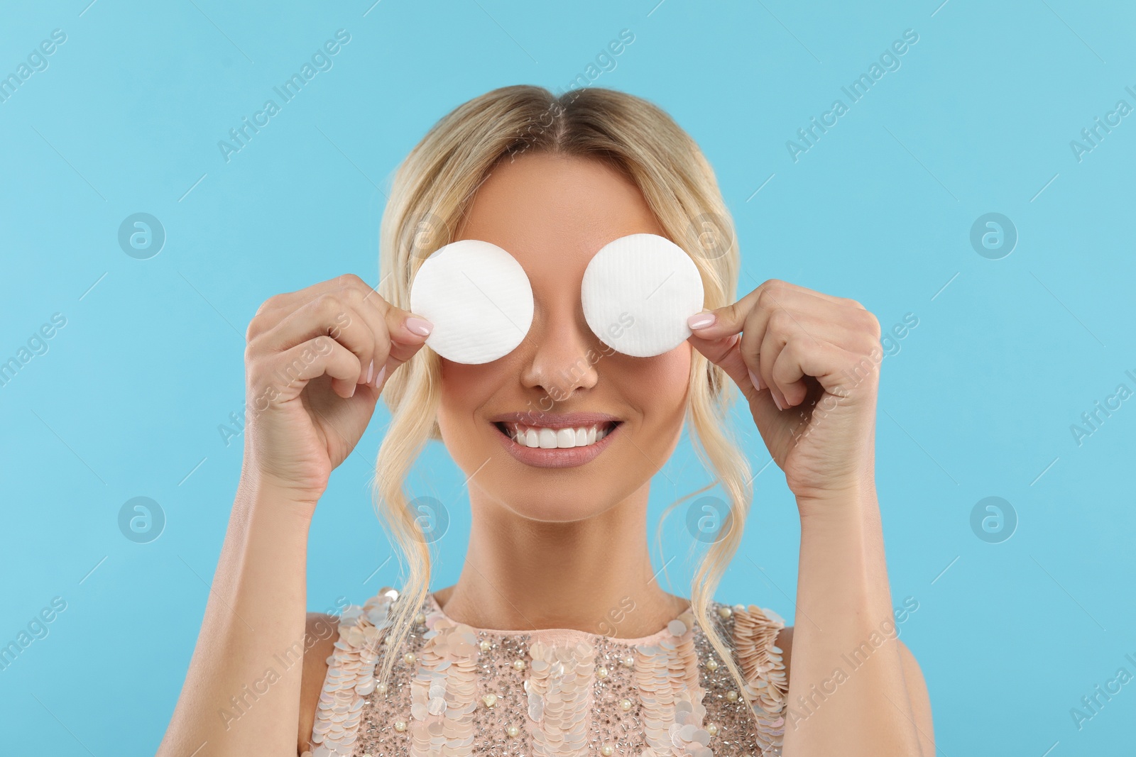 Photo of Smiling woman removing makeup with cotton pads on light blue background