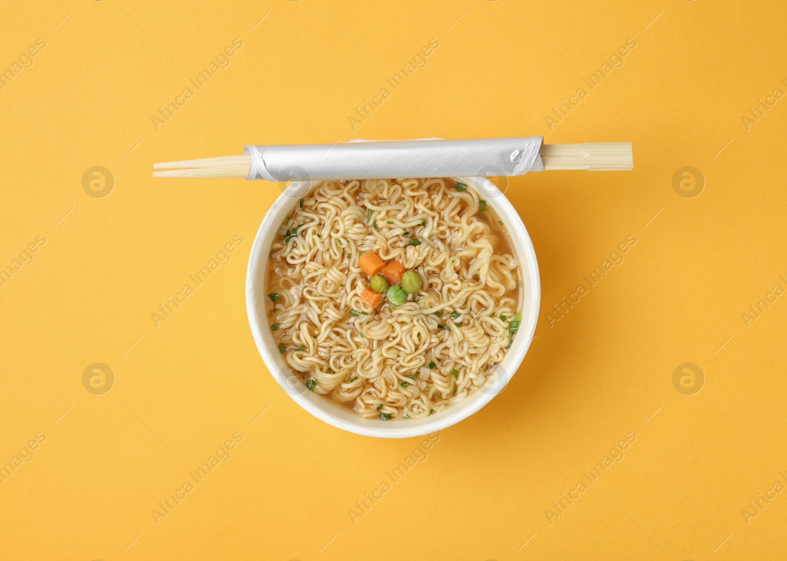 Photo of Cup of cooked instant noodles with chopsticks on color background, top view