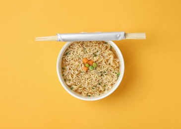 Cup of cooked instant noodles with chopsticks on color background, top view