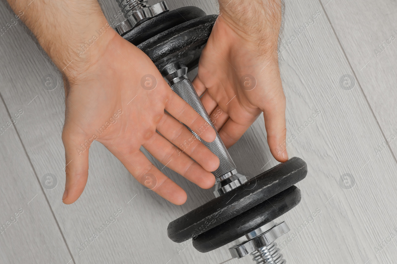 Photo of Sporty man taking dumbbell indoors, closeup. Suffering from calluses on hands