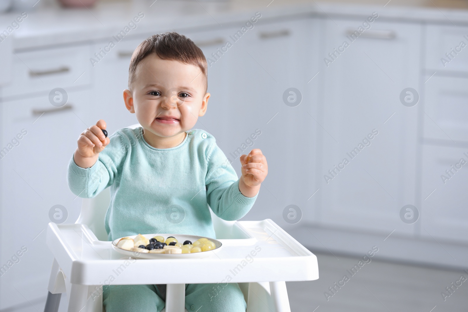 Photo of Cute little baby eating healthy food in high chair at home. Space for text