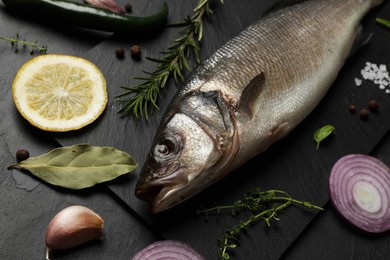 Photo of Sea bass fish and ingredients on black table, closeup