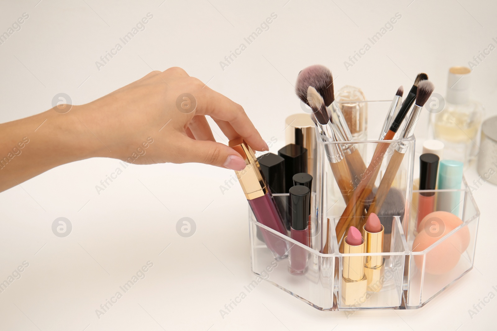 Photo of Woman taking lip gloss from organizer for makeup cosmetic products on dressing table