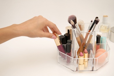 Photo of Woman taking lip gloss from organizer for makeup cosmetic products on dressing table