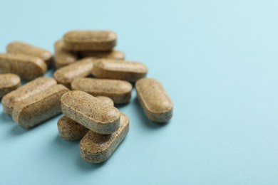 Photo of Dietary supplement pills on light blue background, closeup. Space for text