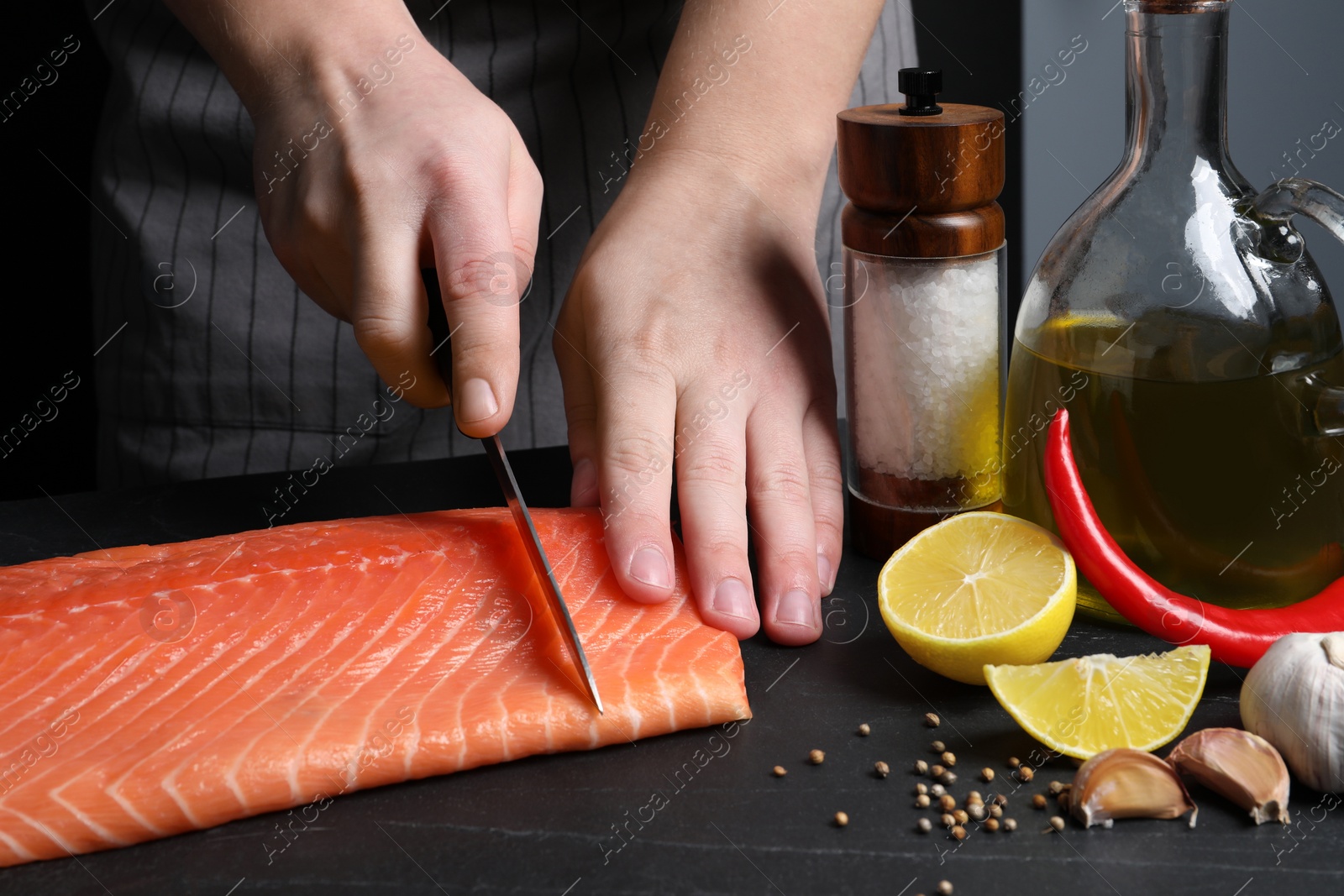 Photo of Man cutting raw salmon at black table, closeup