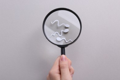Reproductive medicine. Woman looking at sperm cells through magnifier on gray background, top view