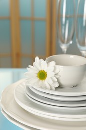 Set of clean dishware and flower on light blue table, closeup