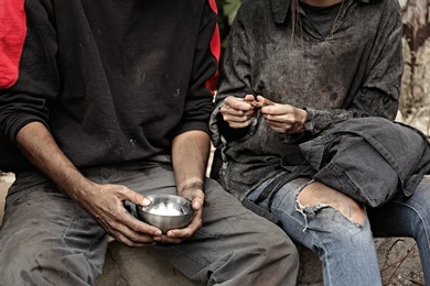 Photo of Poor homeless people sharing piece of bread outdoors, closeup