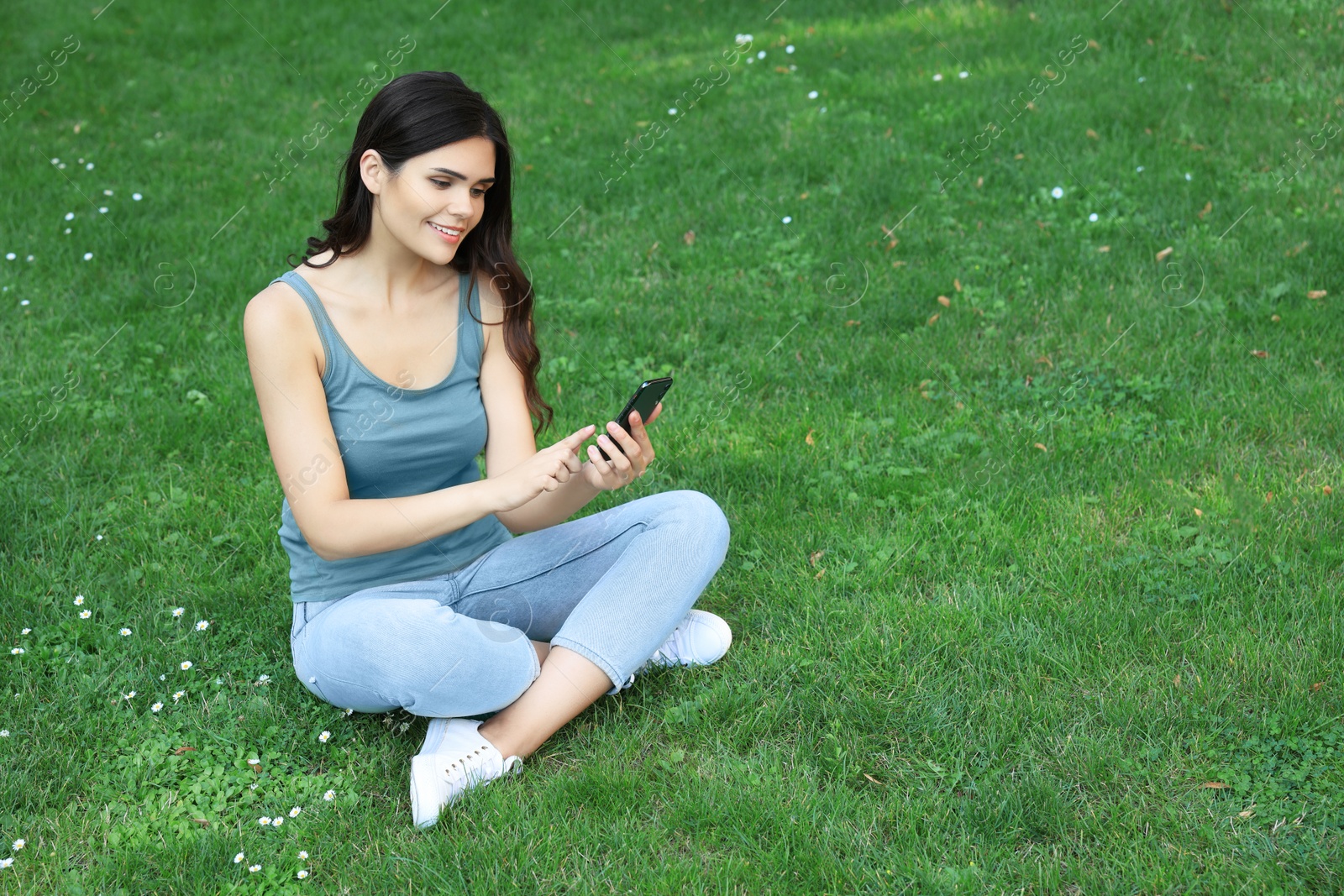 Photo of Young woman using smartphone on green grass outdoors