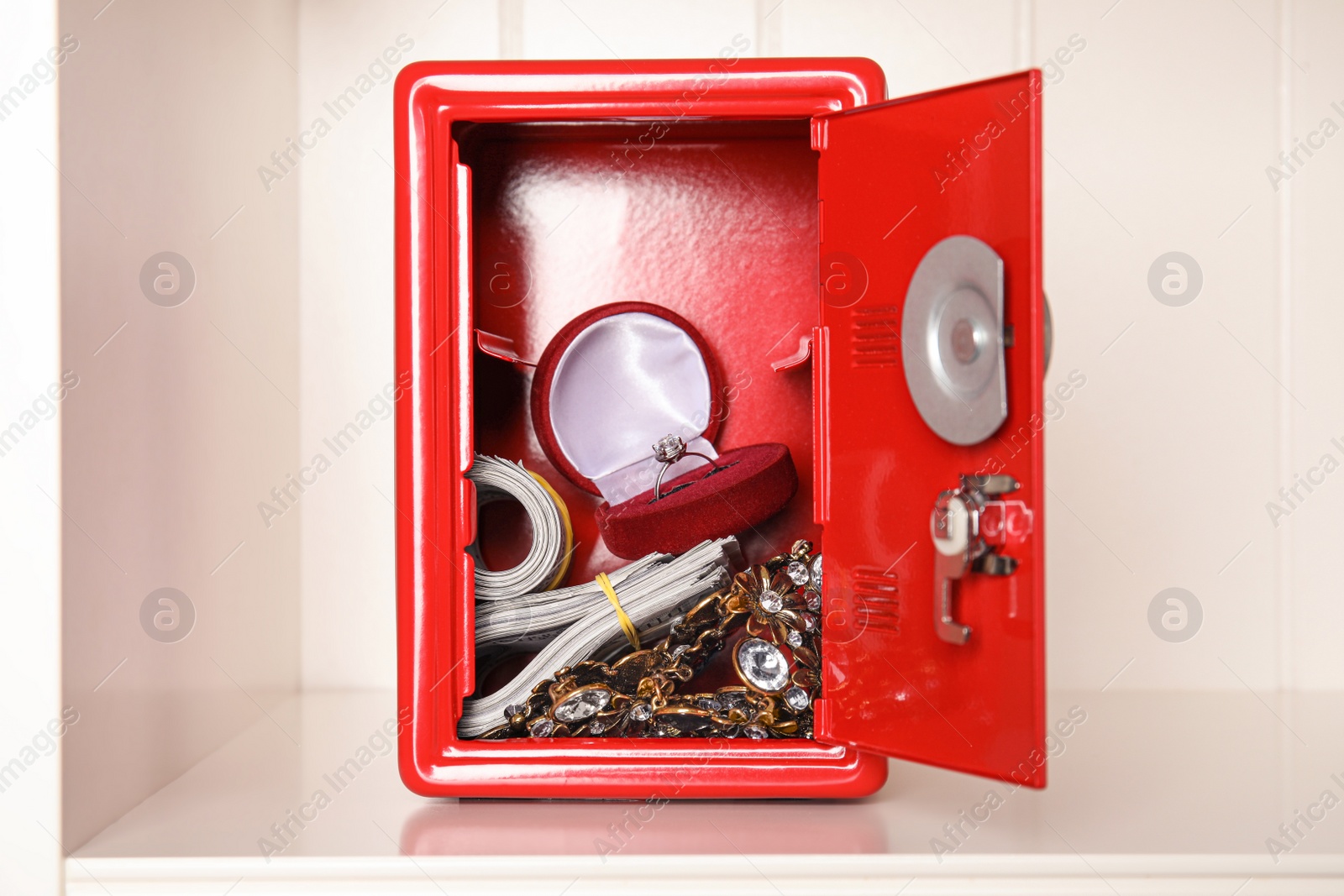 Open red steel safe with money and jewelry on shelf Photo of Open red steel safe with money and jewelry on shelf
