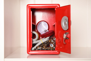 Photo of Open red steel safe with money and jewelry on shelf
