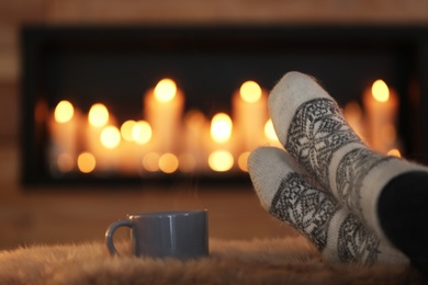 Woman with cup of hot drink on fuzzy rug against blurred background, closeup. Winter atmosphere