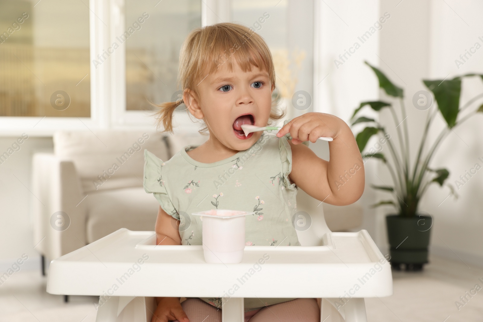 Photo of Cute little child eating tasty yogurt with spoon at home