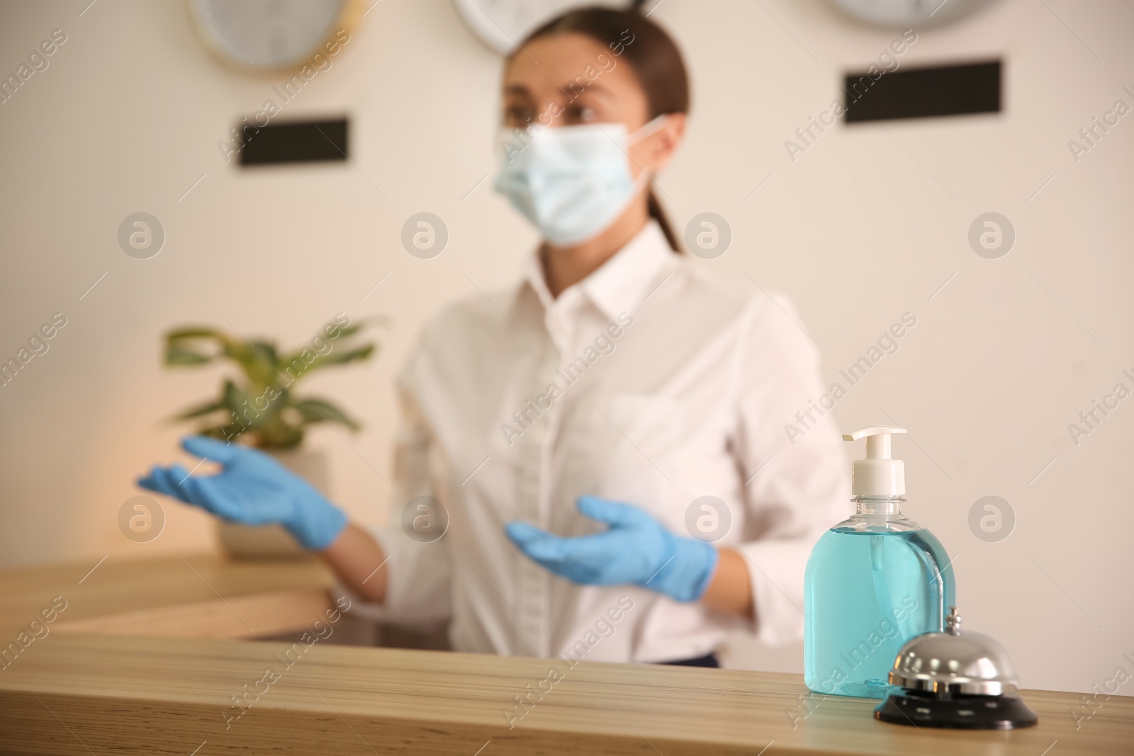 Photo of Receptionist at countertop in hotel, focus on dispenser bottle with antiseptic gel and service bell