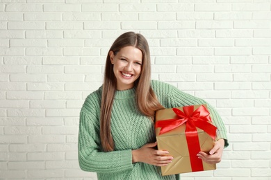 Photo of Happy young woman with Christmas gift near white brick wall