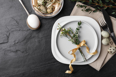 Festive Easter table setting with eggs and floral decoration on dark background, flat lay