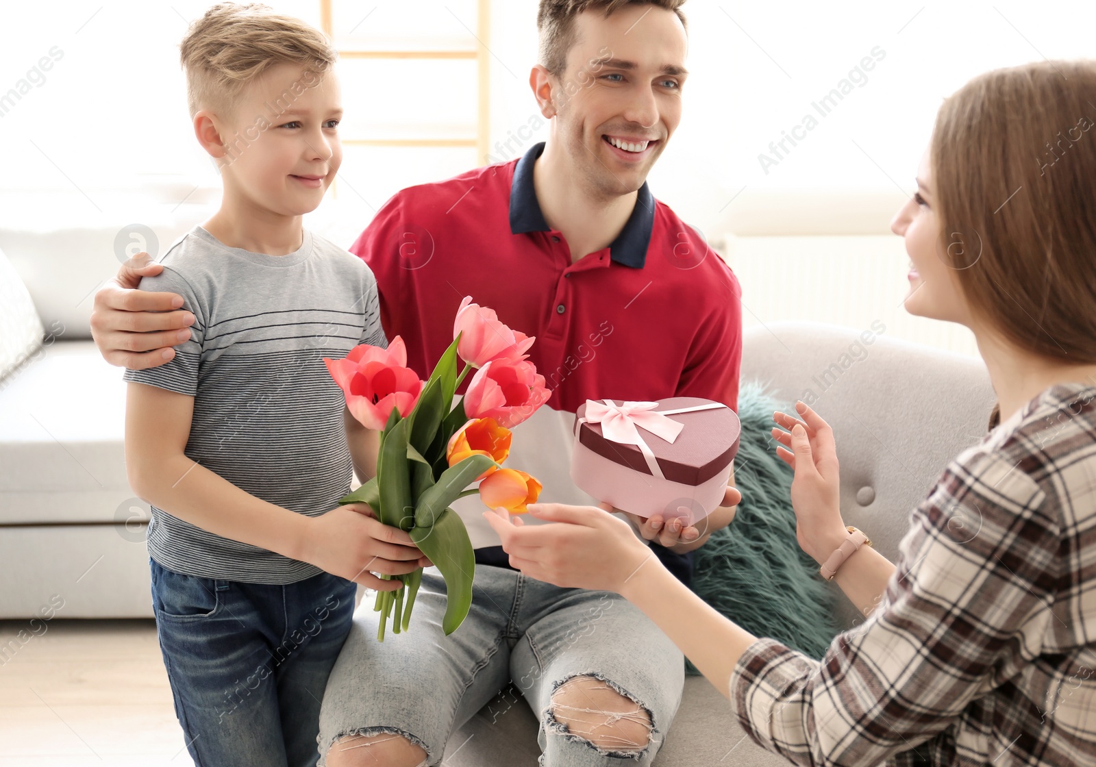 Photo of Happy woman receiving flowers and gift from her family at home. Mother's day celebration