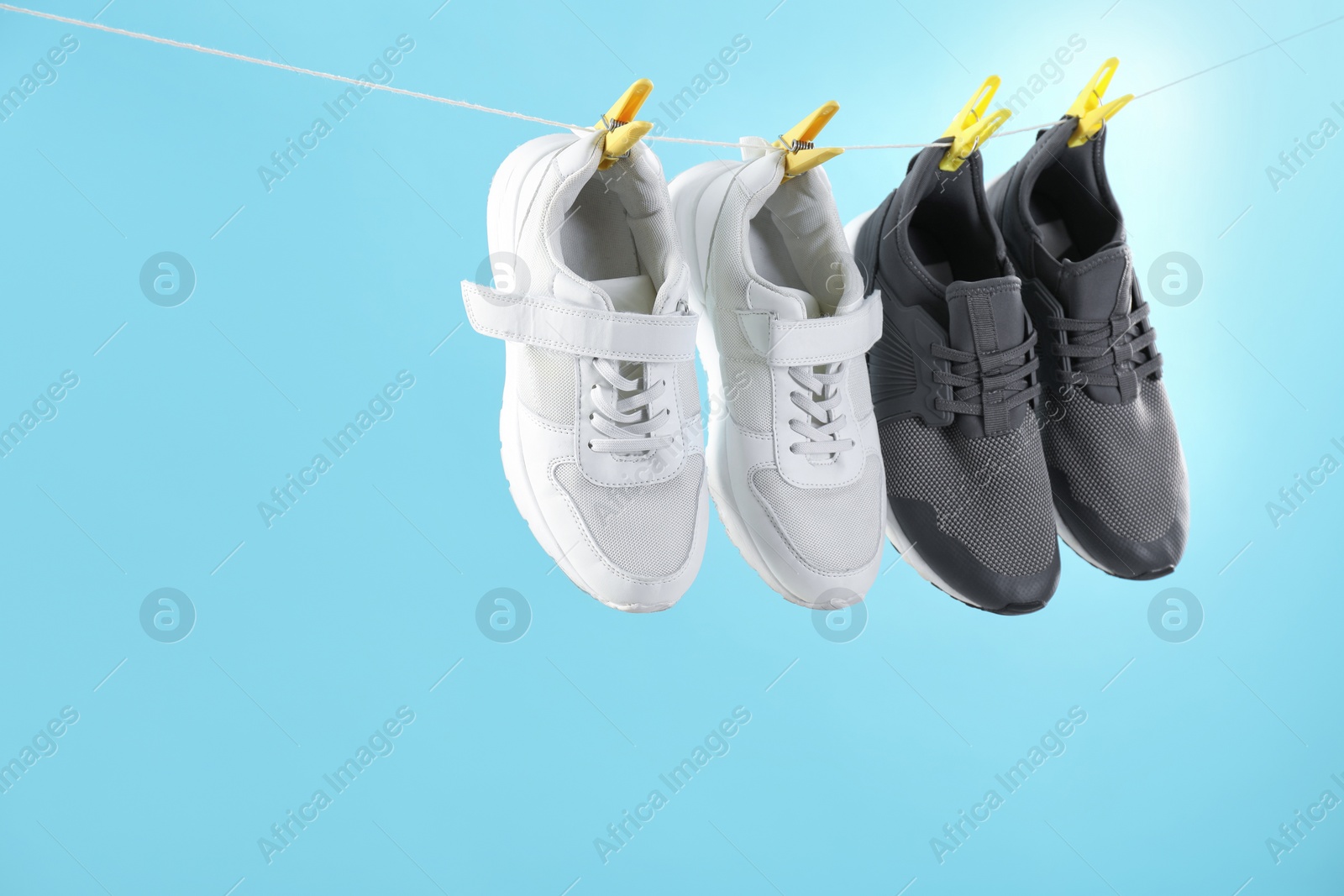 Photo of Different stylish sneakers drying on washing line against light blue background