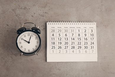 Calendar and alarm clock on grey stone background, flat lay
