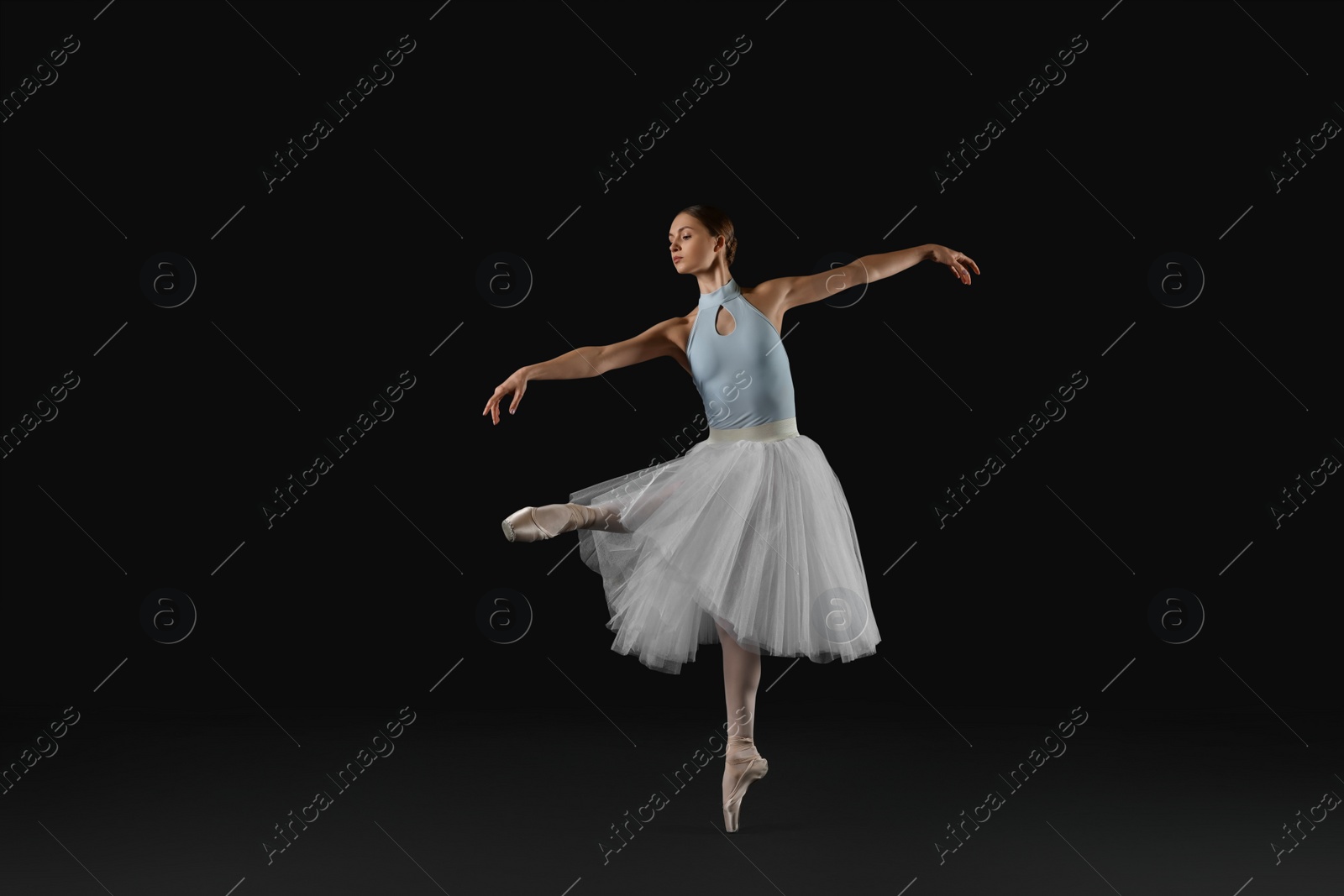 Photo of Young ballerina practicing dance moves on black background