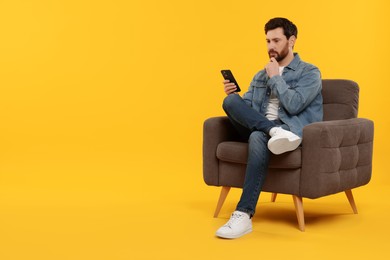 Photo of Handsome man with smartphone sitting on armchair against yellow background. Space for text