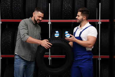 Photo of Mechanic helping client to choose car tire in auto store