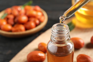 Photo of Dripping jojoba oil from pipette into bottle on blurred background, closeup