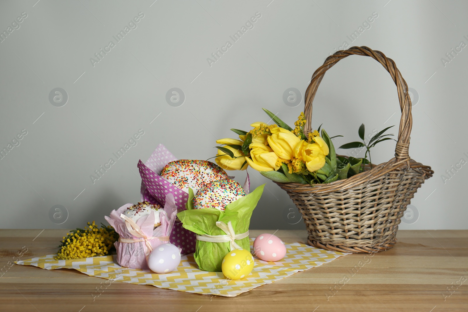 Photo of Delicious Easter cakes, dyed eggs and basket with flowers on wooden table