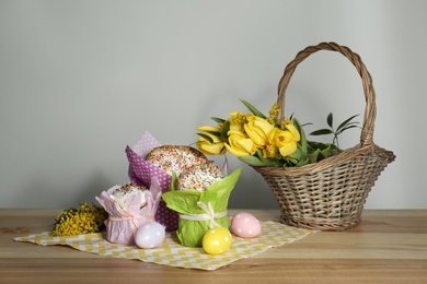 Delicious Easter cakes, dyed eggs and basket with flowers on wooden table