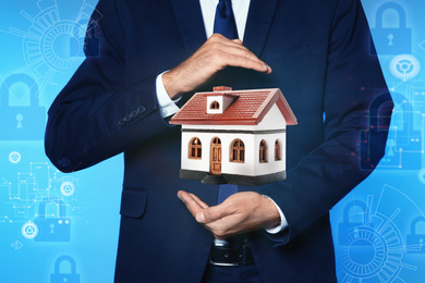 Image of Home security concept. Man holding house on light blue background, closeup