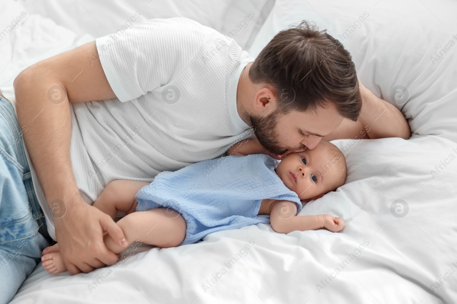 Photo of Father kissing his cute baby on bed indoors