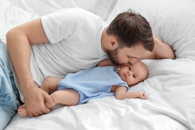 Photo of Father kissing his cute baby on bed indoors