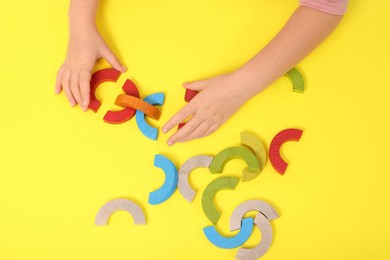 Motor skills development. Girl playing with colorful wooden arcs at yellow table, top view