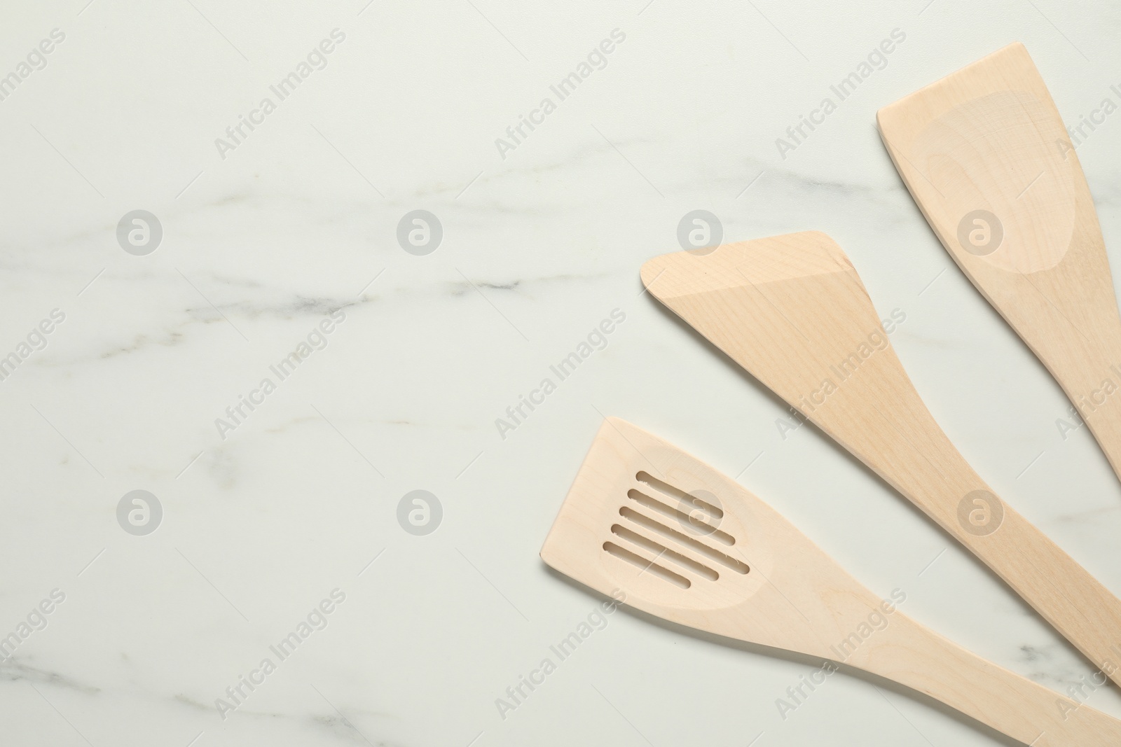 Photo of Different wooden spatulas on white marble table, flat lay. Space for text