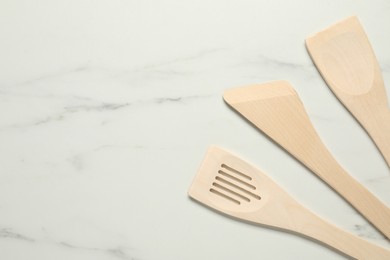 Photo of Different wooden spatulas on white marble table, flat lay. Space for text