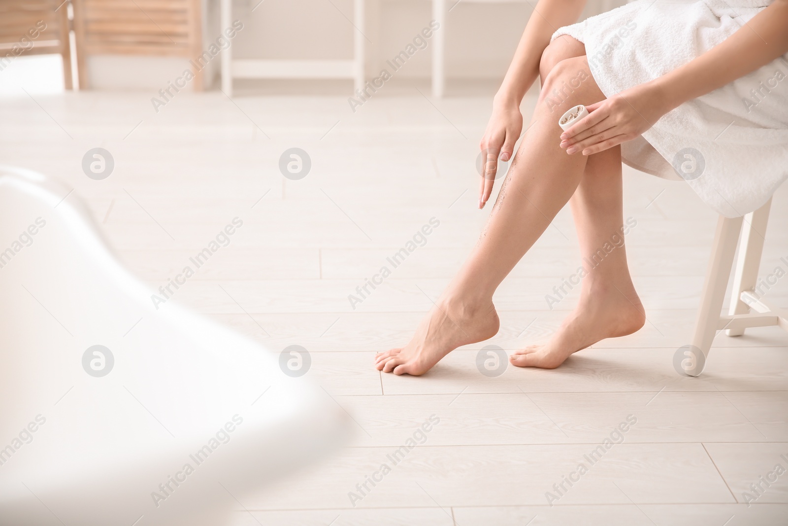 Photo of Woman applying body scrub on legs at home