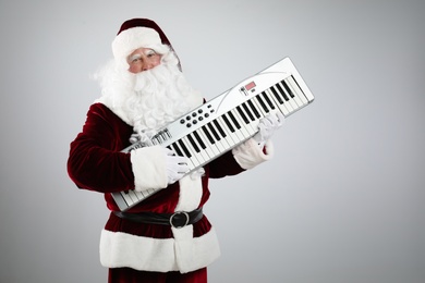 Photo of Santa Claus with synthesizer on light grey background. Christmas music