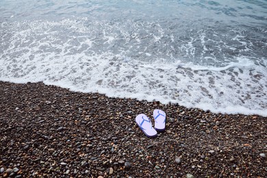 Photo of Stylish lilac flip lops on pebble beach near sea. Space for text