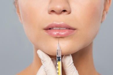 Young woman getting lips injection on grey background, closeup. Cosmetic surgery