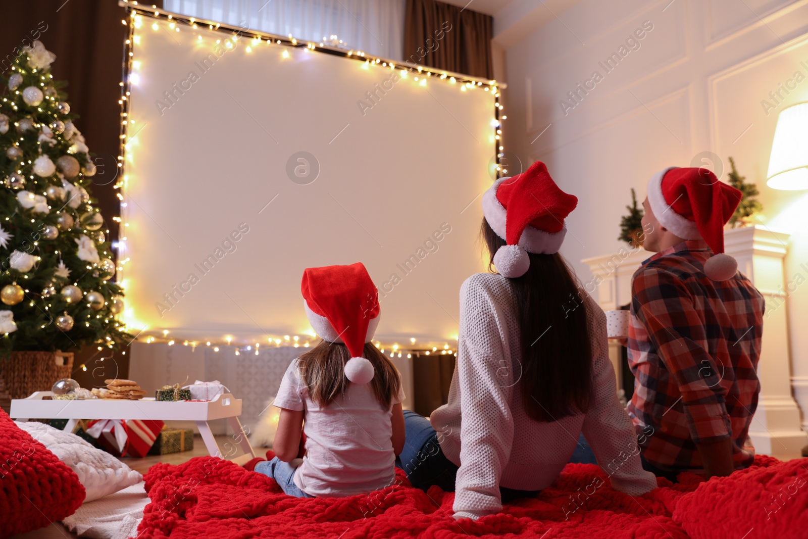 Photo of Family watching movie using video projector at home. Cozy Christmas atmosphere