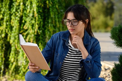 Photo of Young woman reading book outdoors on sunny day