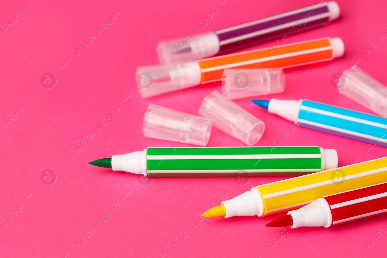 Photo of Many bright markers on pink background, closeup