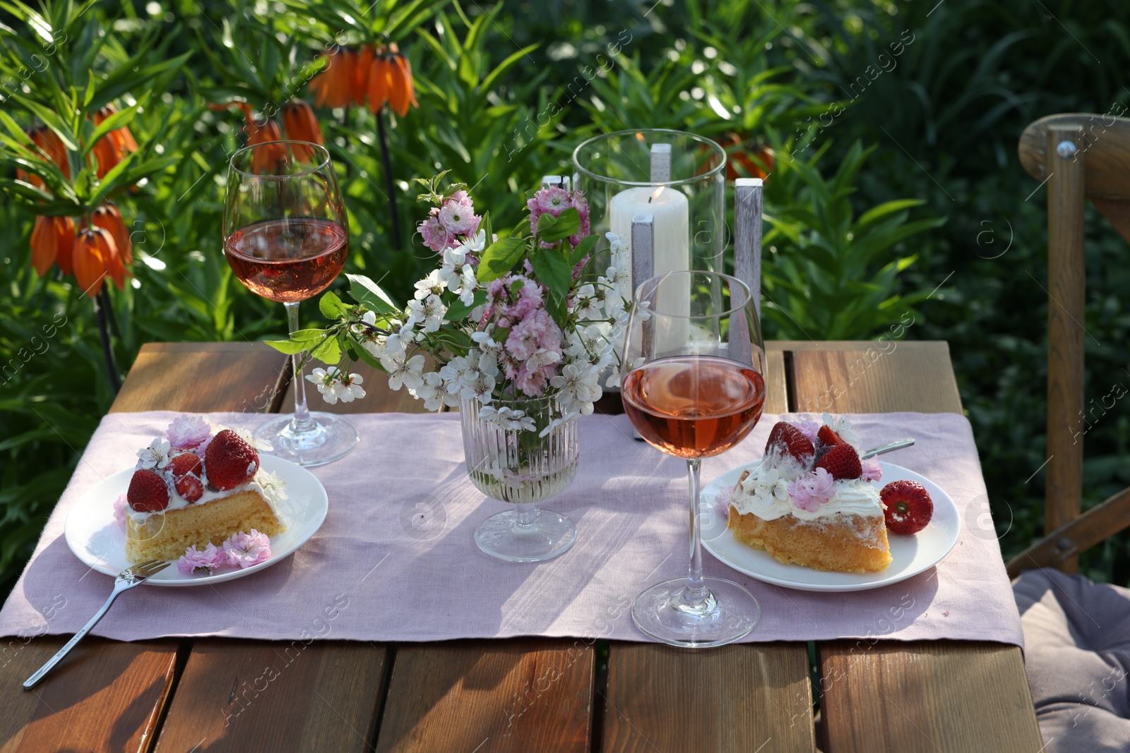 Photo of Vase with spring flowers, wine and cake on table served for romantic date in garden