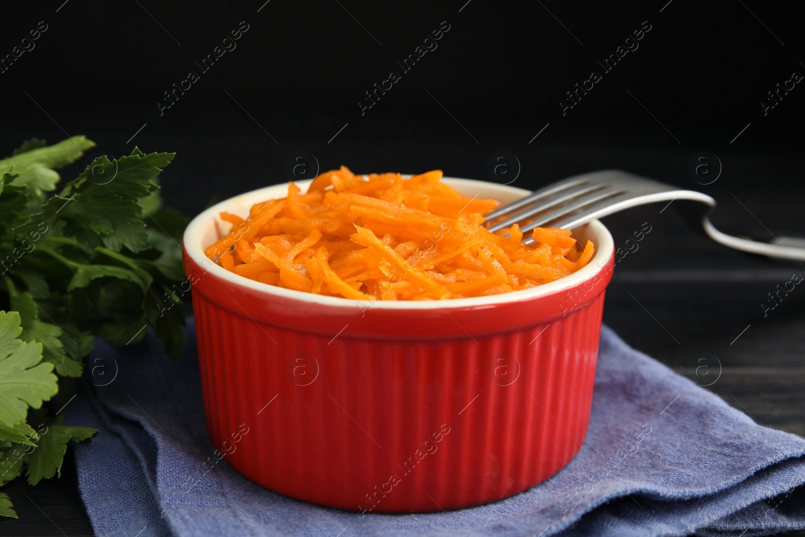 Photo of Delicious Korean carrot salad and parsley on black wooden table