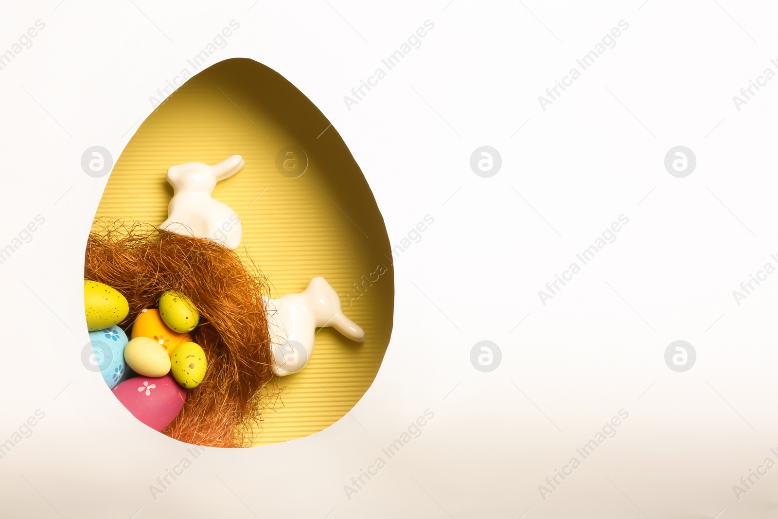 Photo of Top view of composition with Easter bunnies on color background through egg shaped hole, space for text